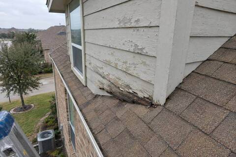 A roof dormer with weathered horizontal boards on its side wall, photographed from a ladder, with the brick first floor and a window far below