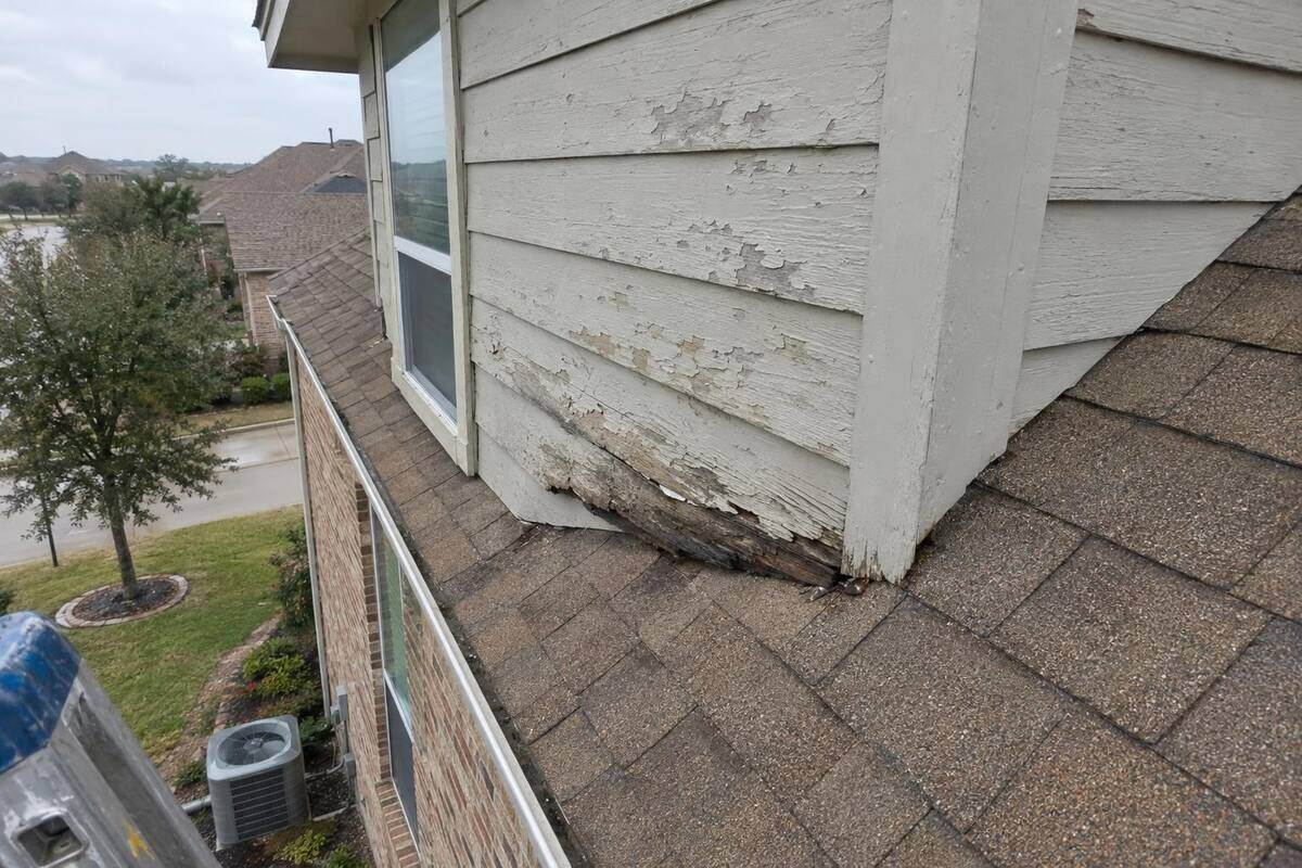 A roof dormer with weathered horizontal boards on its side wall, photographed from a ladder, with the brick first floor and a window far below